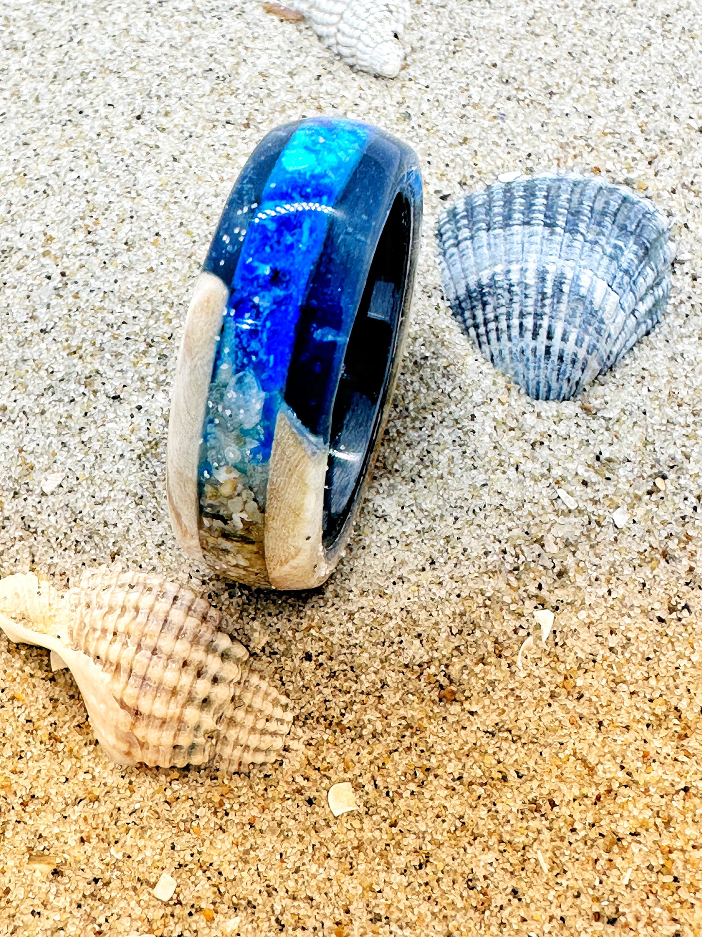 Handgefertigter Ring, gefüllt mit Sand und kleinen Elementen vom Strand. Transparente Harzschicht bewahrt die Struktur des Strandes und macht ihn als tragbare Erinnerung erlebbar.
Handmade ring filled with sand and small elements from the beach. A transparent resin layer preserves the texture of the shore, turning it into a wearable memory.