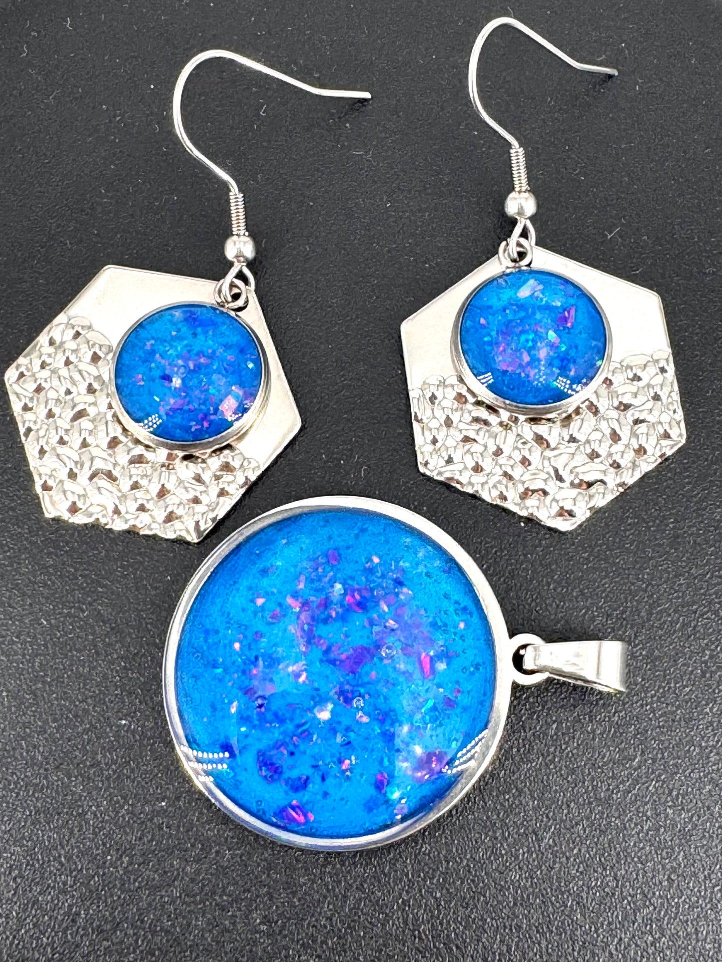 Azure Relic – Schmuckset aus Edelstahl mit Kunstharz und blauen Opalen, bestehend aus rundem Amulett (ca. 4 cm) und passenden Ohrringen. Schimmerndes Blau, eingefangen in metallischem Glanz – ein modernes Relikt aus Licht und Tiefe.