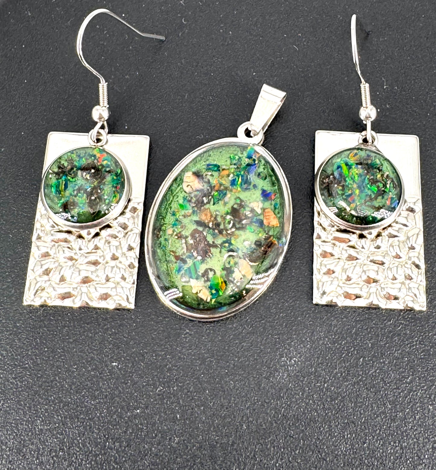 Schmuckset aus Edelstahl mit Kunstharz, Farbpigmenten und schimmernden Opalen – bestehend aus einem ovalen Amulett und passenden Ohrringen. Grüntöne, Kupferreflexe und Lichtspiele verschmelzen zu einem modernen Relikt der Erde