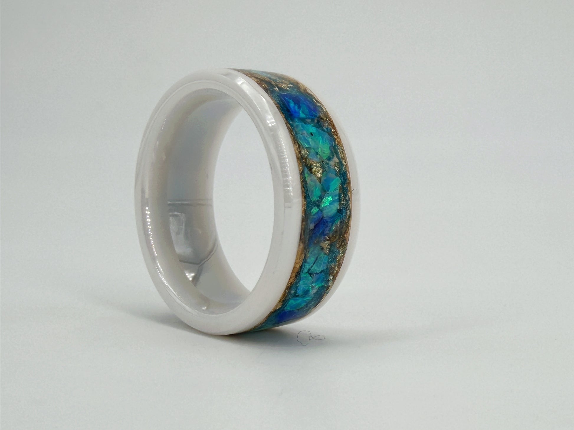 Handgefertigter Ring „Aether Aurum“ aus weißer Keramik mit leuchtend blauen Opalen und goldenen Akzenten. Die Kombination aus Weiß, Blau und Gold erinnert an Himmel, Licht und die Weite des Äthers und verleiht dem Unikat eine elegante, zeitlose Ausstrahlung.