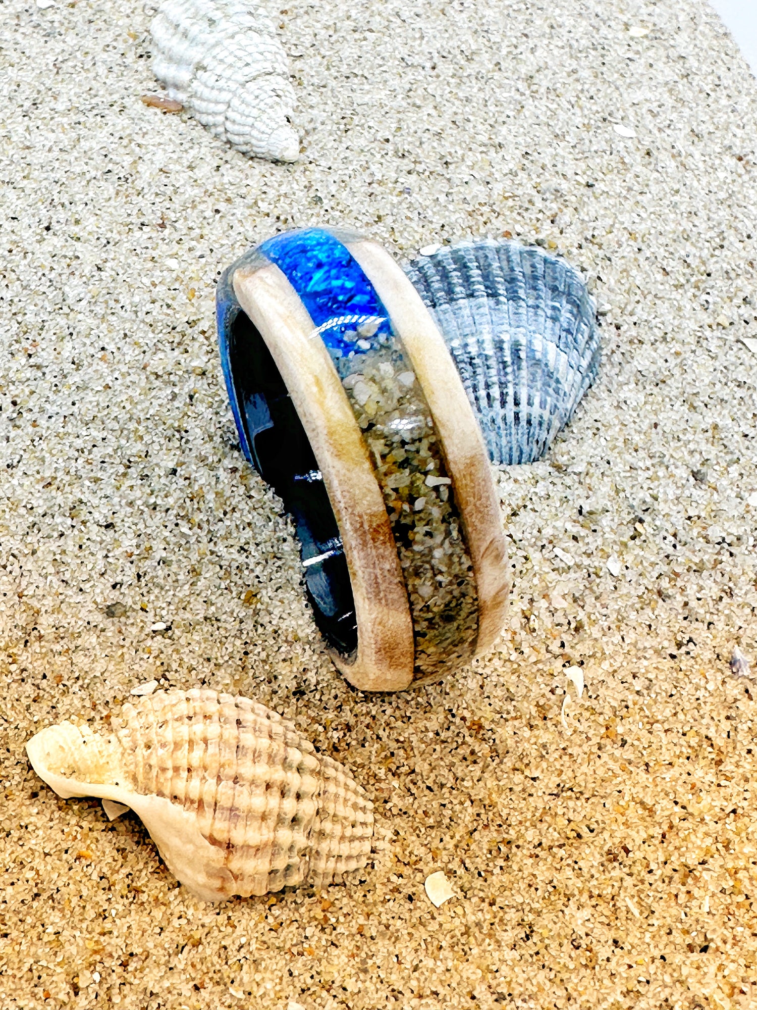 Handgefertigter Ring, gefüllt mit Sand und kleinen Elementen vom Strand. Transparente Harzschicht bewahrt die Struktur des Strandes und macht ihn als tragbare Erinnerung erlebbar.

Handmade ring filled with sand and small elements from the beach. A transparent resin layer preserves the texture of the shore, turning it into a wearable memory.