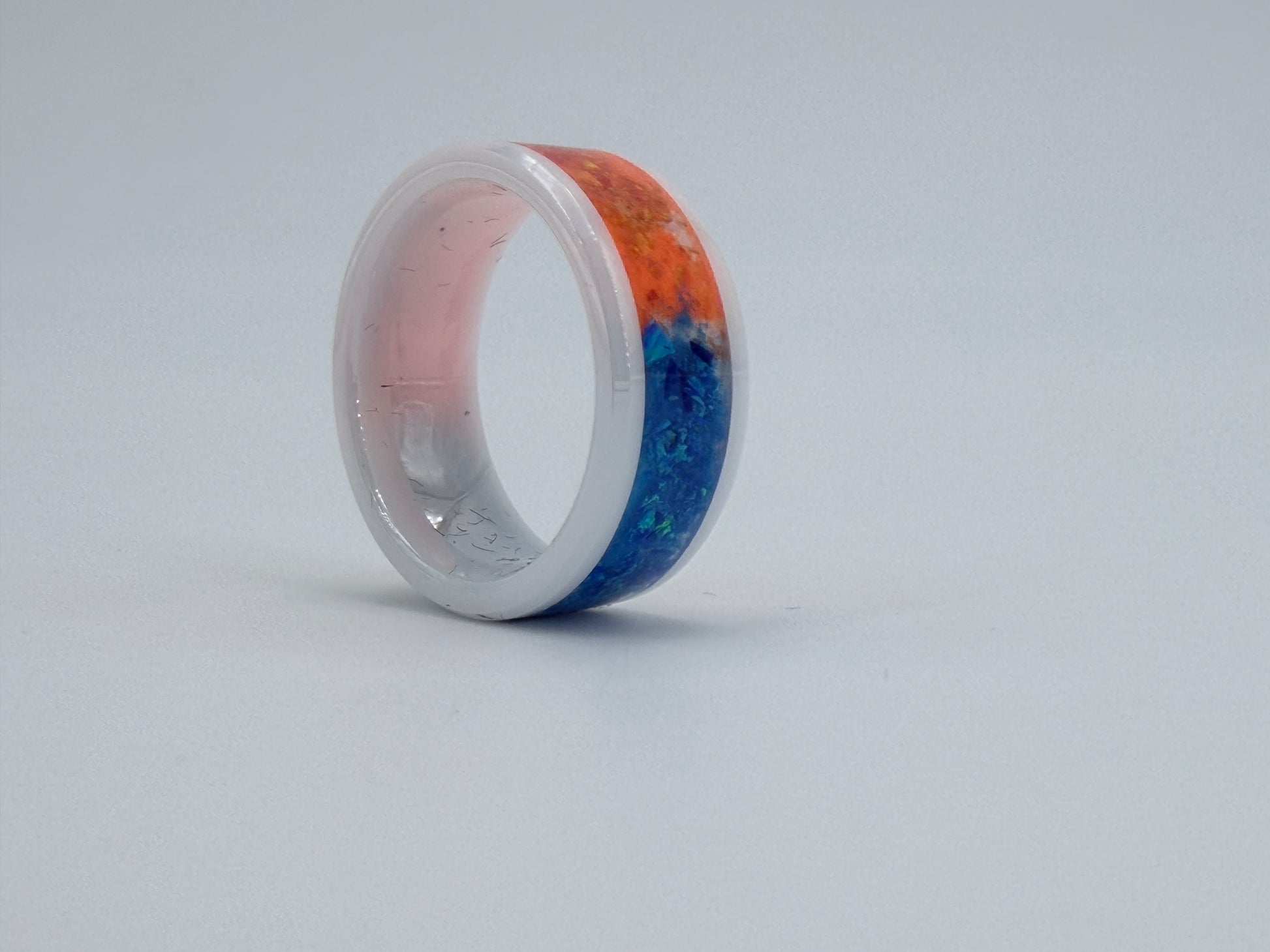 Ring „Horizon“ aus weißer Keramik mit blauen und orangenen Opalen, handgefertigt im Atelier Artinrings.