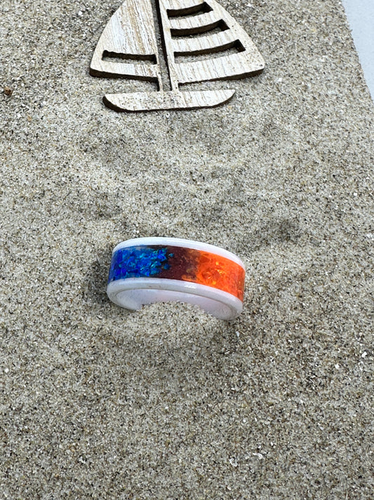 Ring aus weisser Keramik, eine Hälfte gefüllt mit blauen opalen, die andere Hälfte mit orangenen Opalen.