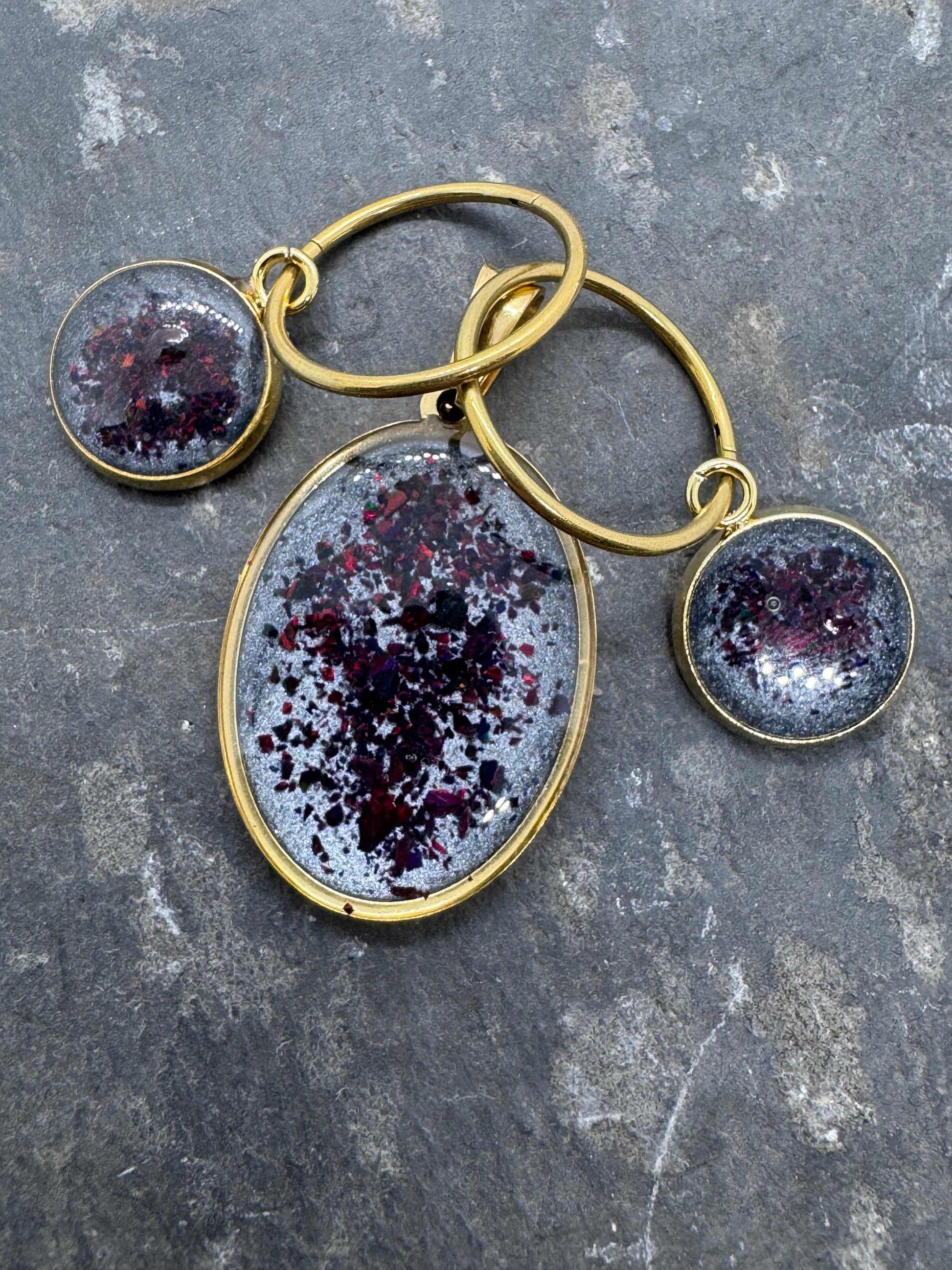 Schmuckset aus Ohrringen und Amulett in Edelstahl. Rote Opale eingefangen auf einem Background aus grauen Pigmenten
