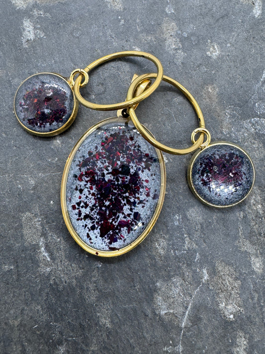 Schmuckset aus Ohrringen und Amulett in Edelstahl. Rote Opale eingefangen auf einem Background aus grauen Pigmenten