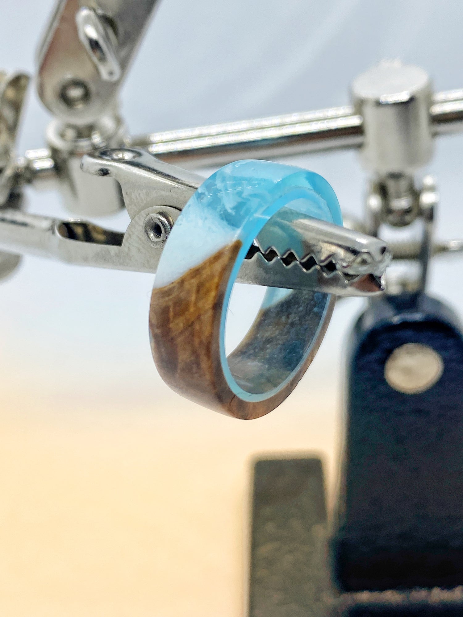 Schmaler Ring aus Kunstharz und Holz, 5 mm breit. In transparentem Harz erscheinen helle Blautöne und braune Holzstrukturen, die sich harmonisch miteinander verbinden.  Alt-Text (EN): Slim ring made of resin and wood, 5 mm wide. Transparent resin reveals light blue tones and natural brown wood patterns, blending together in a unique design.