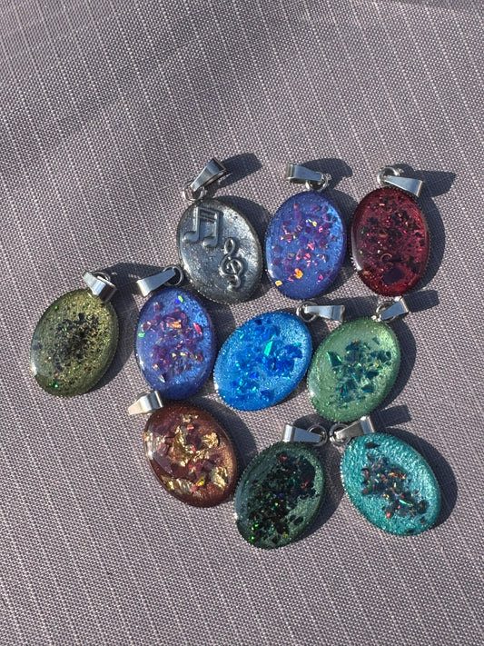 Mehrere handgefertigte Amulette, jeweils etwa 2 cm groß, in verschiedenen Farben und Materialien. Die kleinen Anhänger zeigen individuelle Muster und wirken als farbenfrohe, tragbare Kunstwerke.

Several handmade amulets, each about 2 cm in size, in different colors and materials. The small pendants display unique patterns, appearing as colorful pieces of wearable art.
