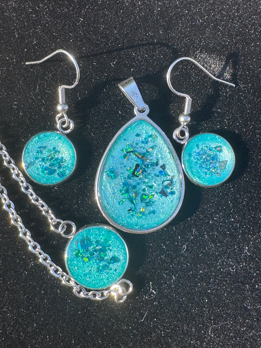Handgefertigtes Schmuckset in Türkis, bestehend aus Ohrringen, einem Amulett und einem Armband. Die intensiven Türkistöne wirken frisch und lebendig und machen das Set zu einem harmonischen Ensemble.

Handmade turquoise jewelry set including earrings, an amulet and a bracelet. The vibrant turquoise tones create a fresh and lively look, forming a harmonious ensemble.
