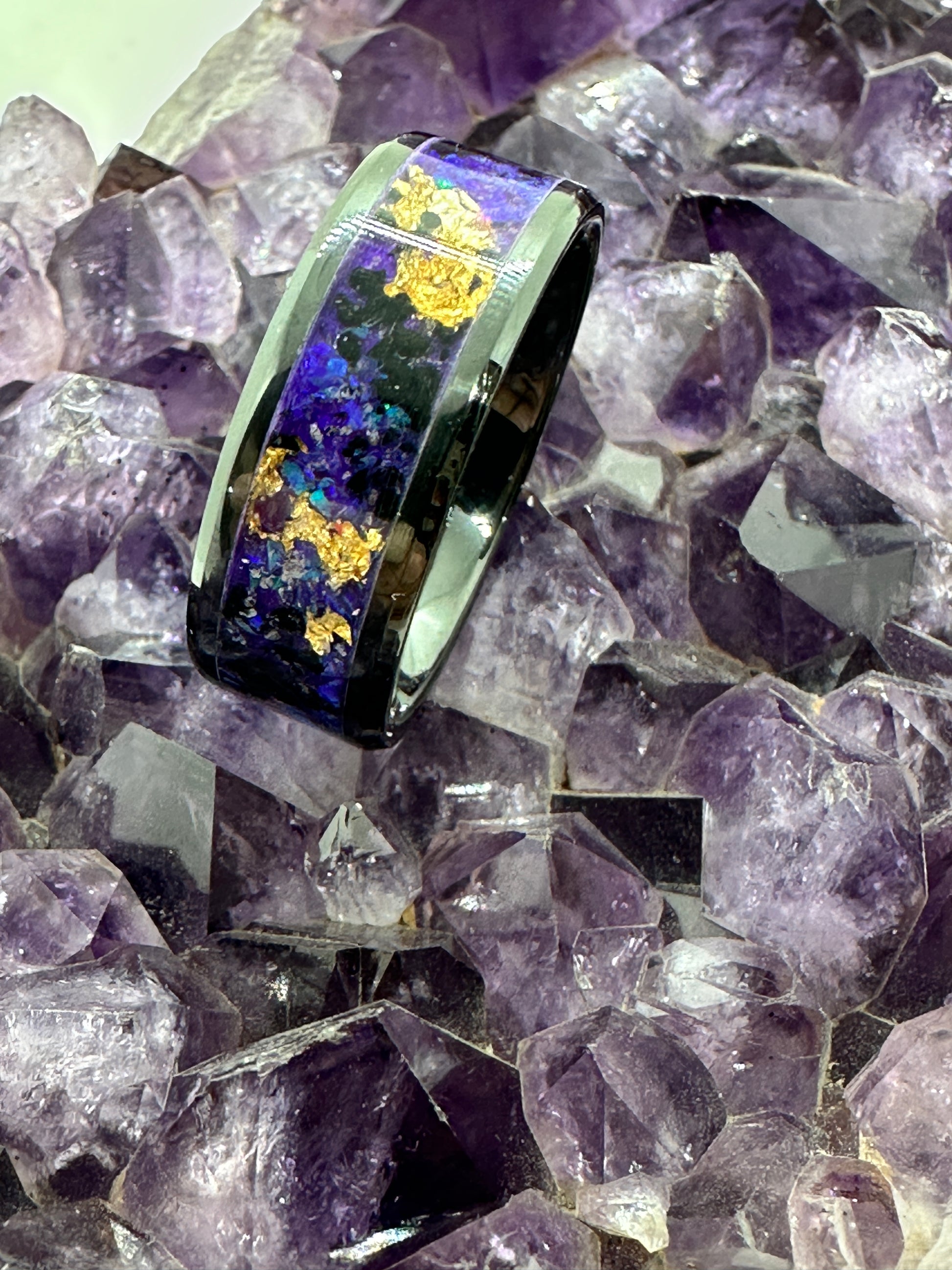 Handgefertigter Ring New Orleans, mit goldfarbenen Elementen, inszeniert auf einer Amethystdruse. Der Kontrast zwischen schimmerndem Gold und den violetten Kristallen des Amethysts verstärkt die mystische Ausstrahlung des Schmuckstücks.

Handmade New Orleans ring with golden elements, displayed on an amethyst druse. The contrast between the shimmering gold and the violet crystals of the amethyst enhances the mystical aura of the jewel.