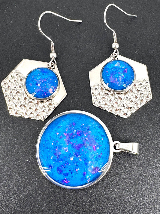 Azure Relic – Schmuckset aus Edelstahl mit Kunstharz und blauen Opalen, bestehend aus rundem Amulett (ca. 4 cm) und passenden Ohrringen. Schimmerndes Blau, eingefangen in metallischem Glanz – ein modernes Relikt aus Licht und Tiefe.