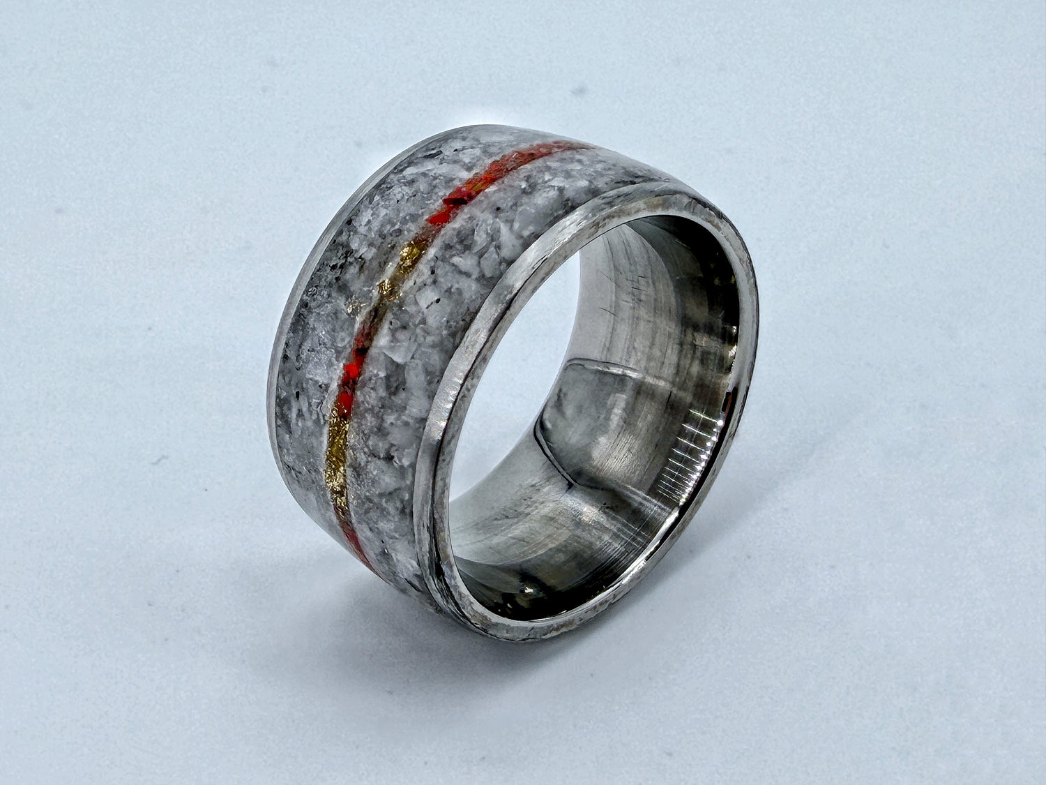 Contemporary ring sculpture with grey textured surface and a red and gold inlay line, symbolizing the path of violence.