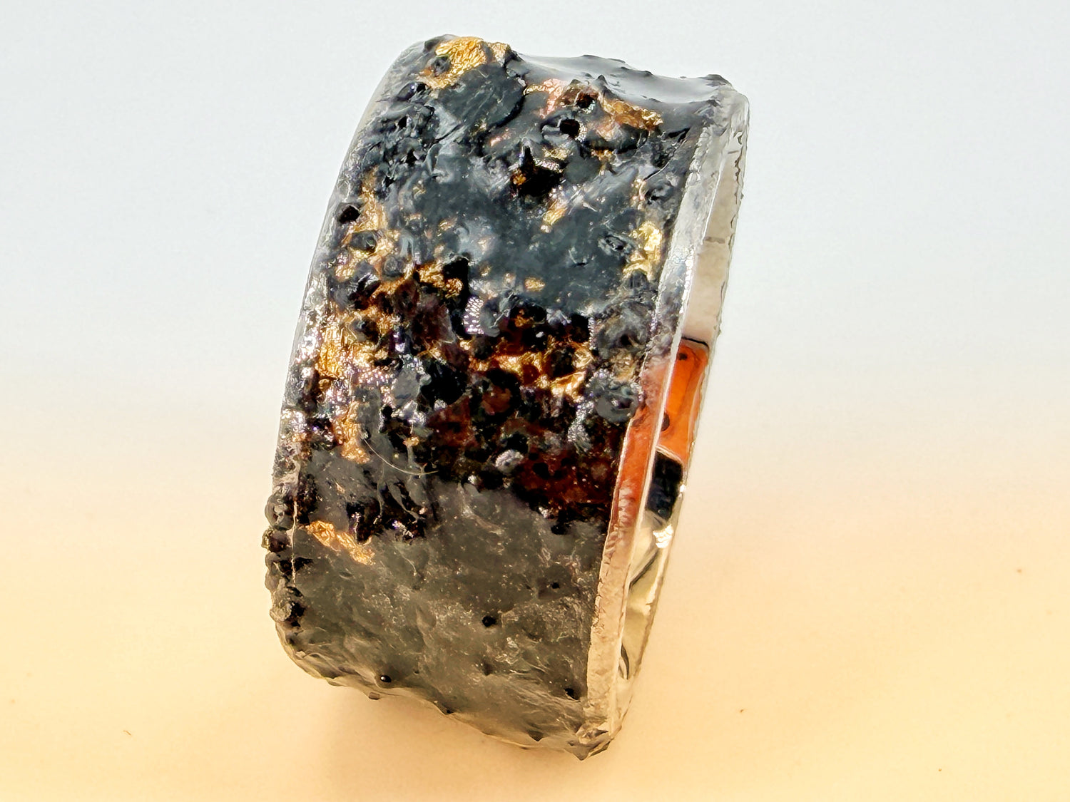 Dunkle Mixed-Media-Ring­skulptur „War“ aus der Serie Apokalyptische Reiter – strukturierte schwarze Materialien mit roten Akzenten in einer Stahlfassung.