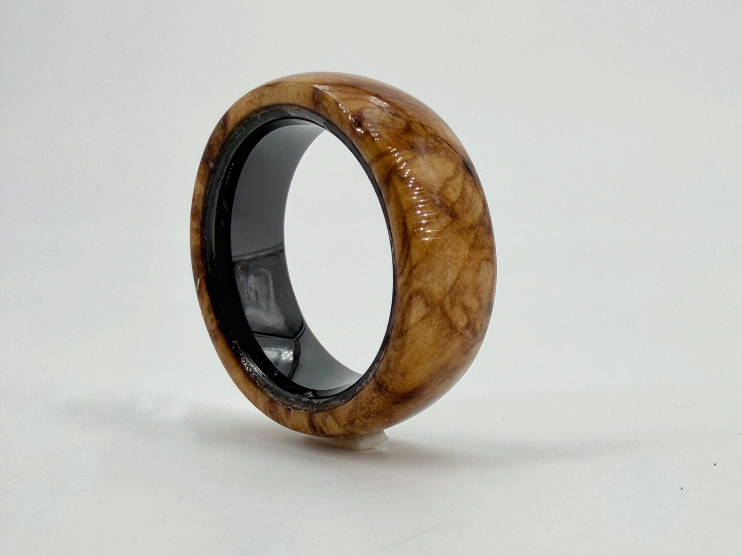 Handgefertigter Ring aus Olivenholz mit markanter Maserung und warmer goldbrauner Farbgebung. Jedes Stück ist ein Unikat und bewahrt die natürliche Schönheit jahrhundertealter Olivenbäume.